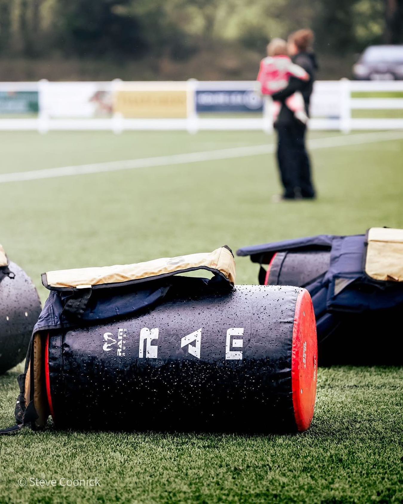 Black and red sports bag with 'Ram Rugby' branding on a grass field, people in the background.