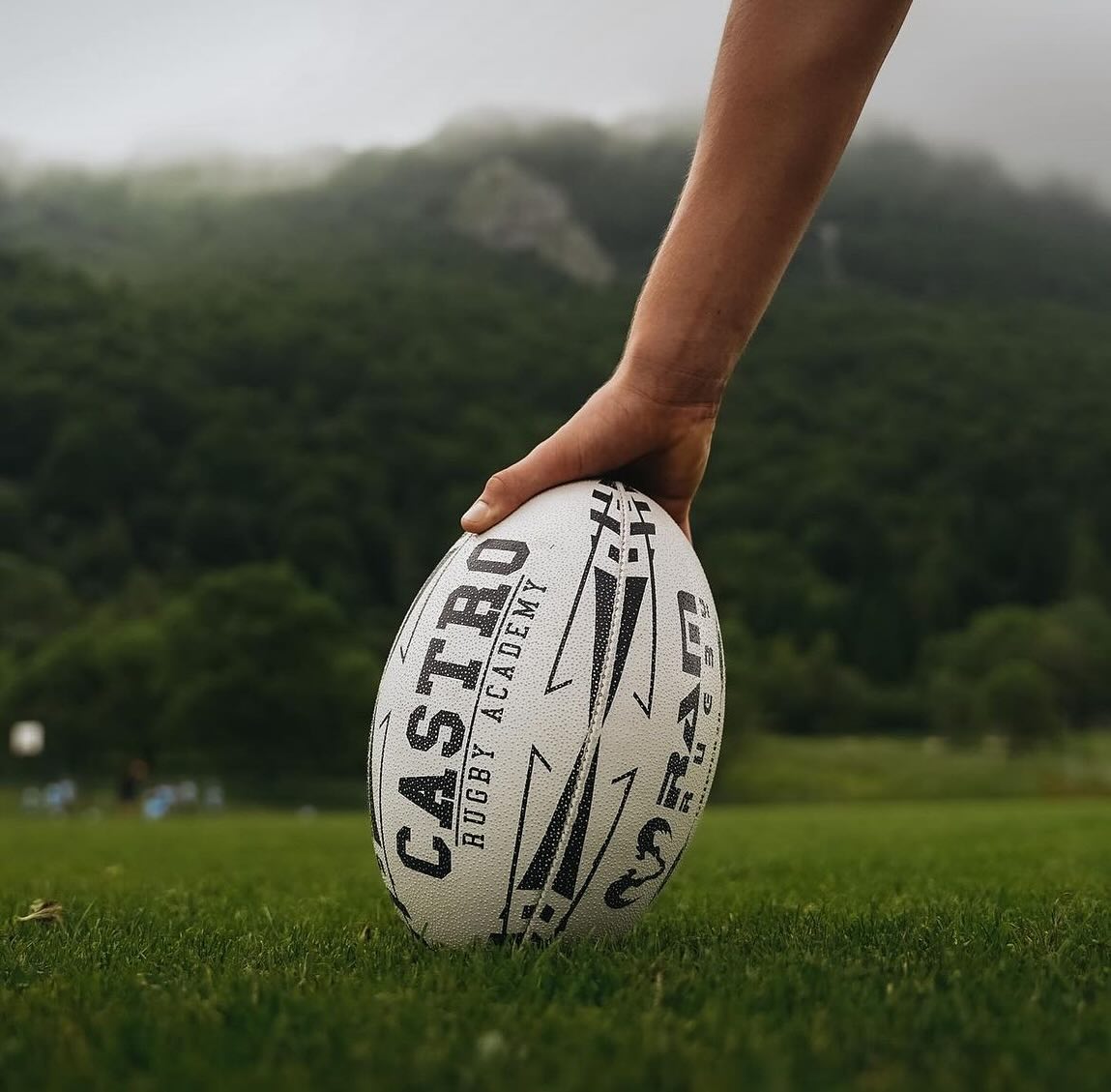 Man holding a Ram Rugby ball on a grass field